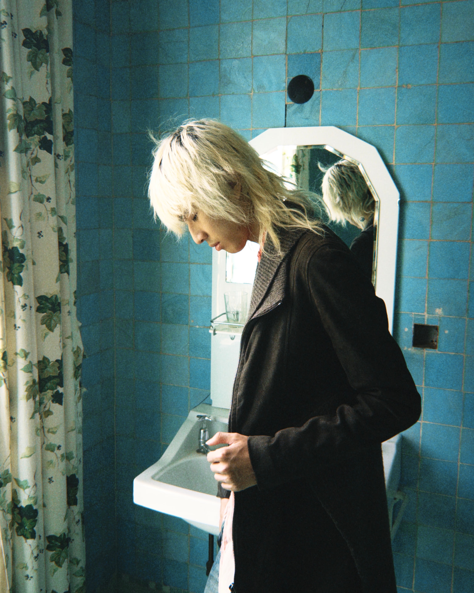 Lan standing quietly by a sink in a blue-tiled bathroom