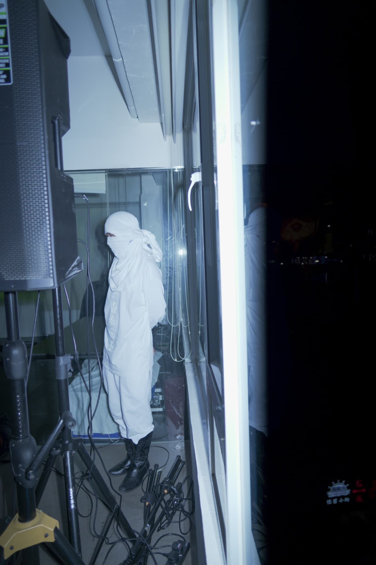 Holy Yam in an all-white robe standing by a dark window