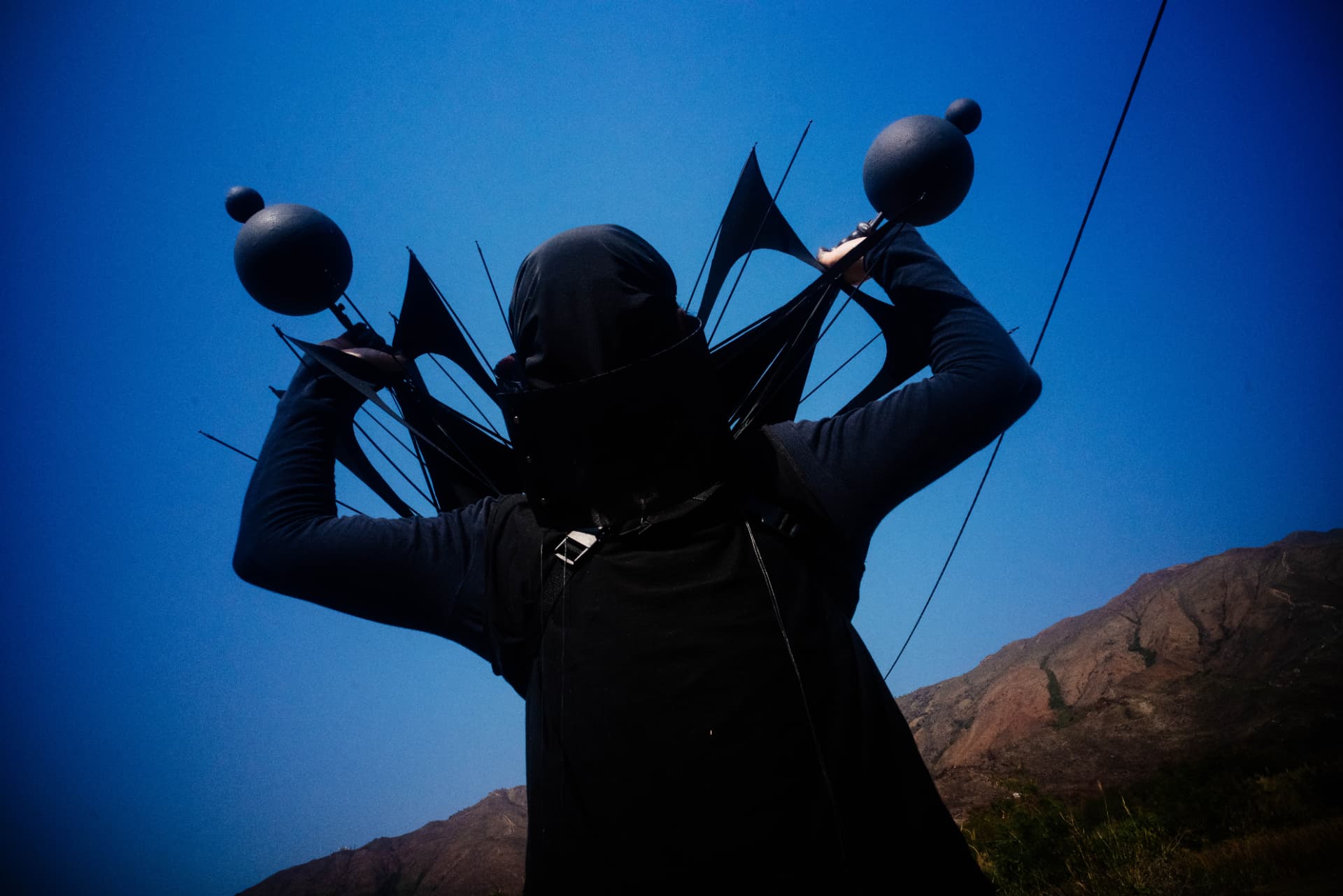 Holy Yam carrying a spiky umbrella rig over his shoulders against a deep blue sky