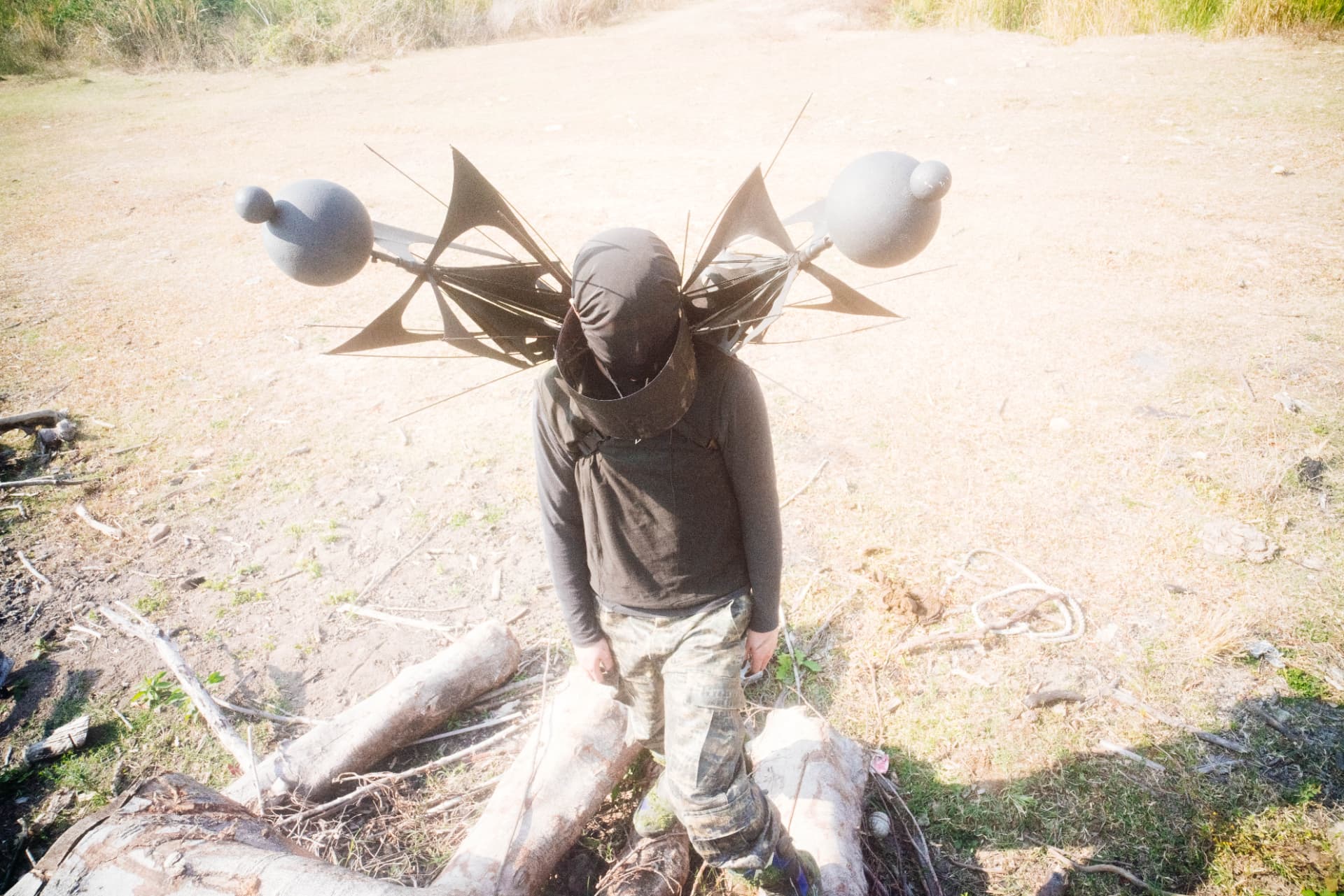 Holy Yam in camouflage walking through a dry field carrying his umbrella rig